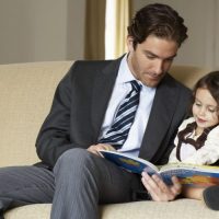 businessman-father-reading-to-daughter-on-sofa